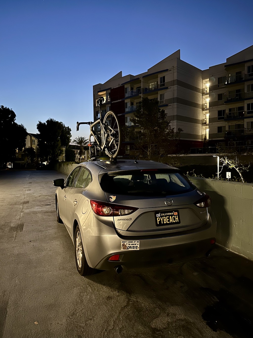 bicycle mounted on the roof of a car parked between apartment buildings