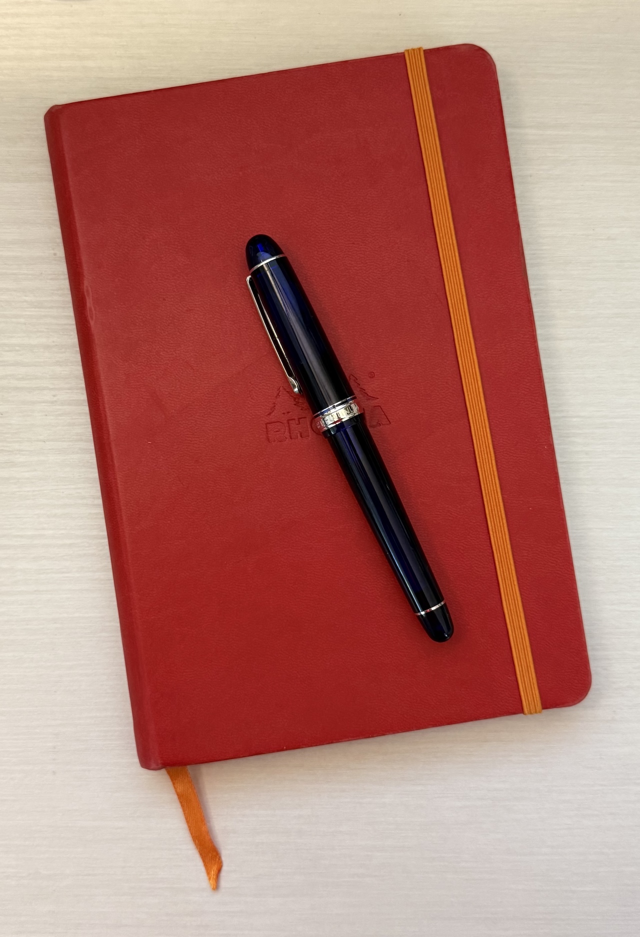 Platinum 3776 Century fountain pen in blue with gold accents on a red Rhodia Rhodiarama Webnotebook with an orange closure and and ribbon bookmark
